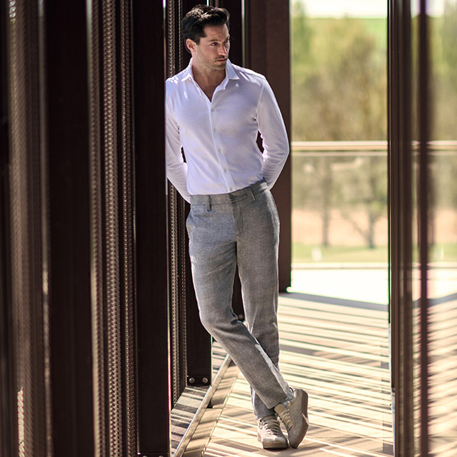 Mann in weißem Freizeithemd und grauer Leinenhose im Freien stehend