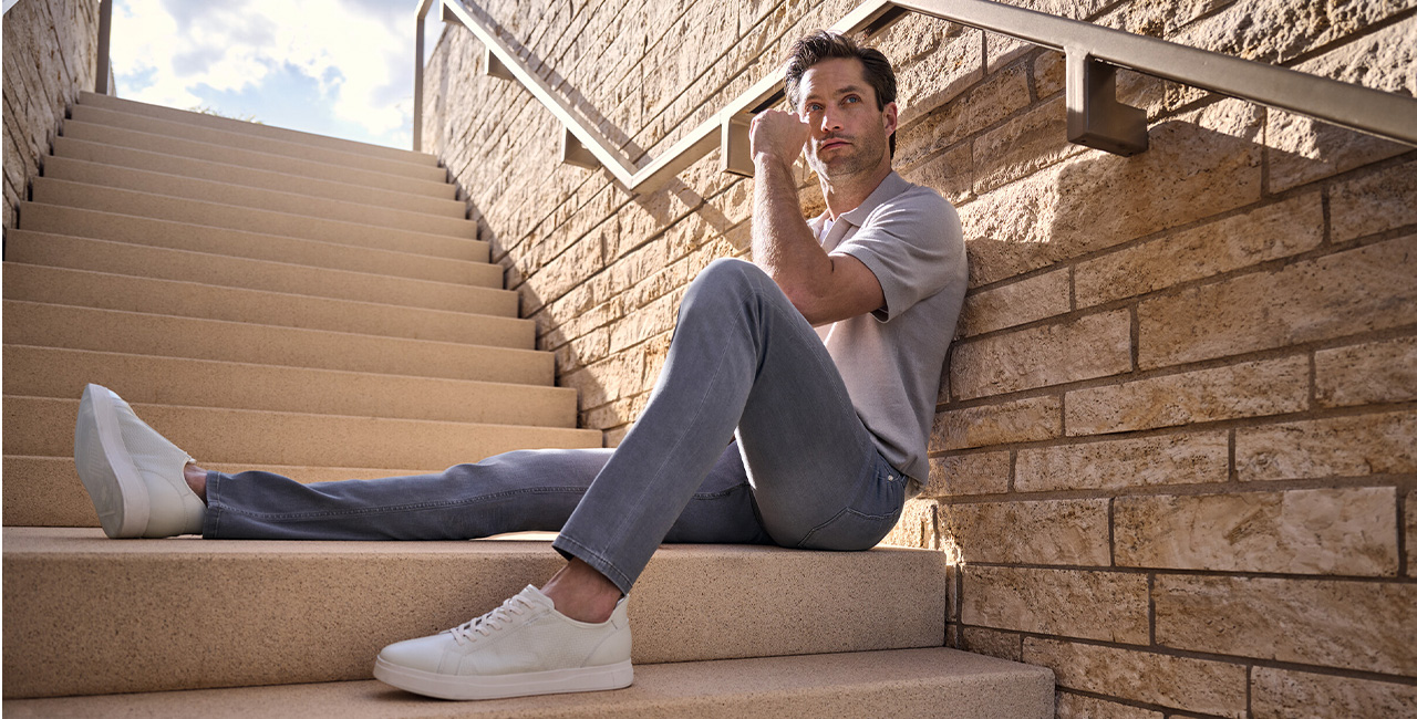 Mann in grauem T-Shirt und hellblauer Jeans, weiße Sneakers, lässig auf Treppe sitzend