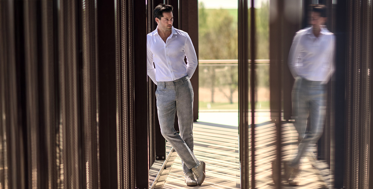 Mann in weißem Hemd und grauer Chino, lässig an Wand lehnend