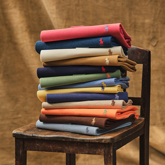 Gefaltete Poloshirts in verschiedenen Farben, auf einem Stuhl gestapelt, aus Baumwolle