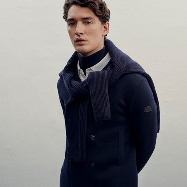 Mann in dunkelblauem Mantel mit Schal und weißem Hemd, elegant präsentiert