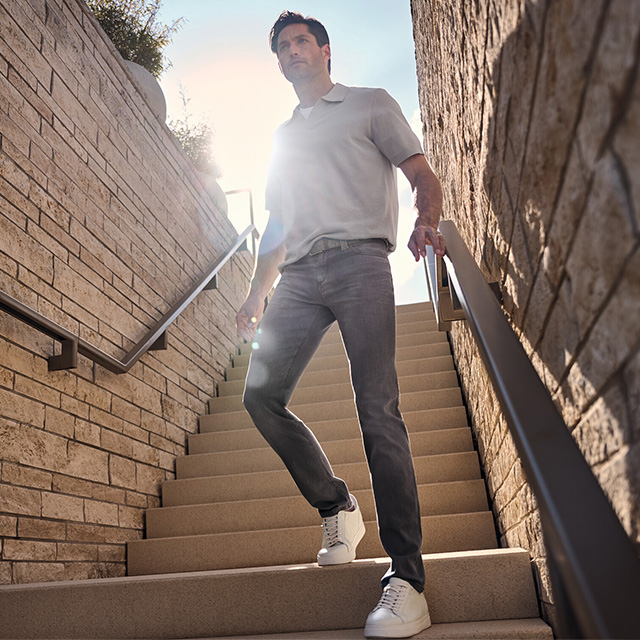 Graue Jeans und weißes Poloshirt, Mann geht Treppe hinauf bei Sonnenlicht
