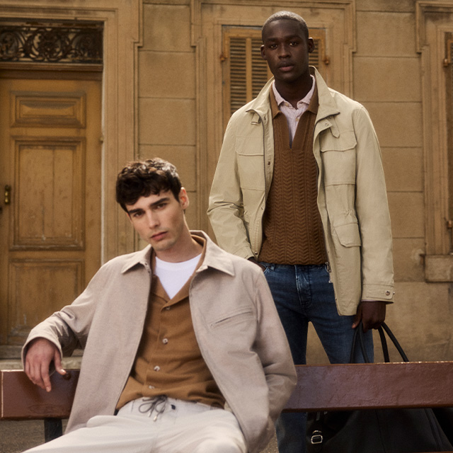 Herren in beiger Jacke und braunem Strickpullover, getragen mit Jeans im städtischen Umfeld