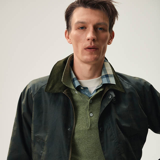 Mann in olivgrüner Jacke und kariertem Hemd, lässig im Studio getragen