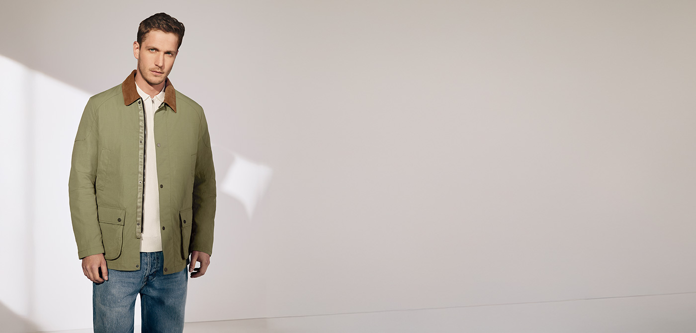 Grüne Herrenjacke mit braunem Kragen über weißem Shirt, klassisch geschnitten, lässig mit Jeans kombiniert.