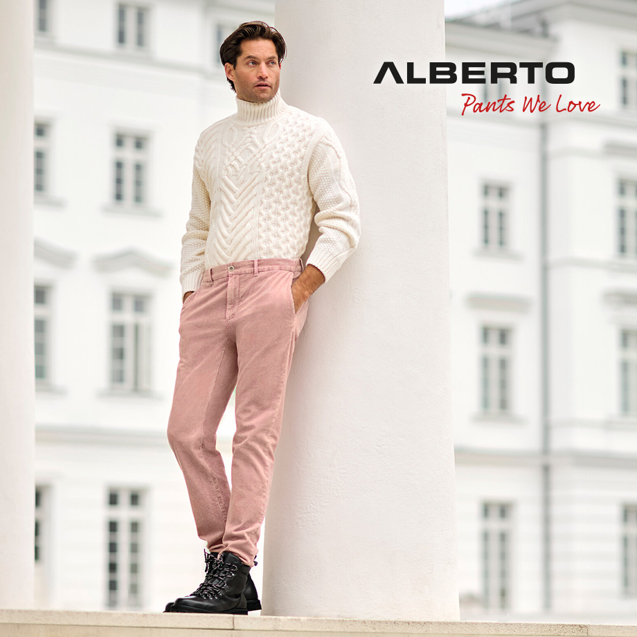 Mann in weißem Strickpullover und rosa Stoffhose, leger an Säule lehnend