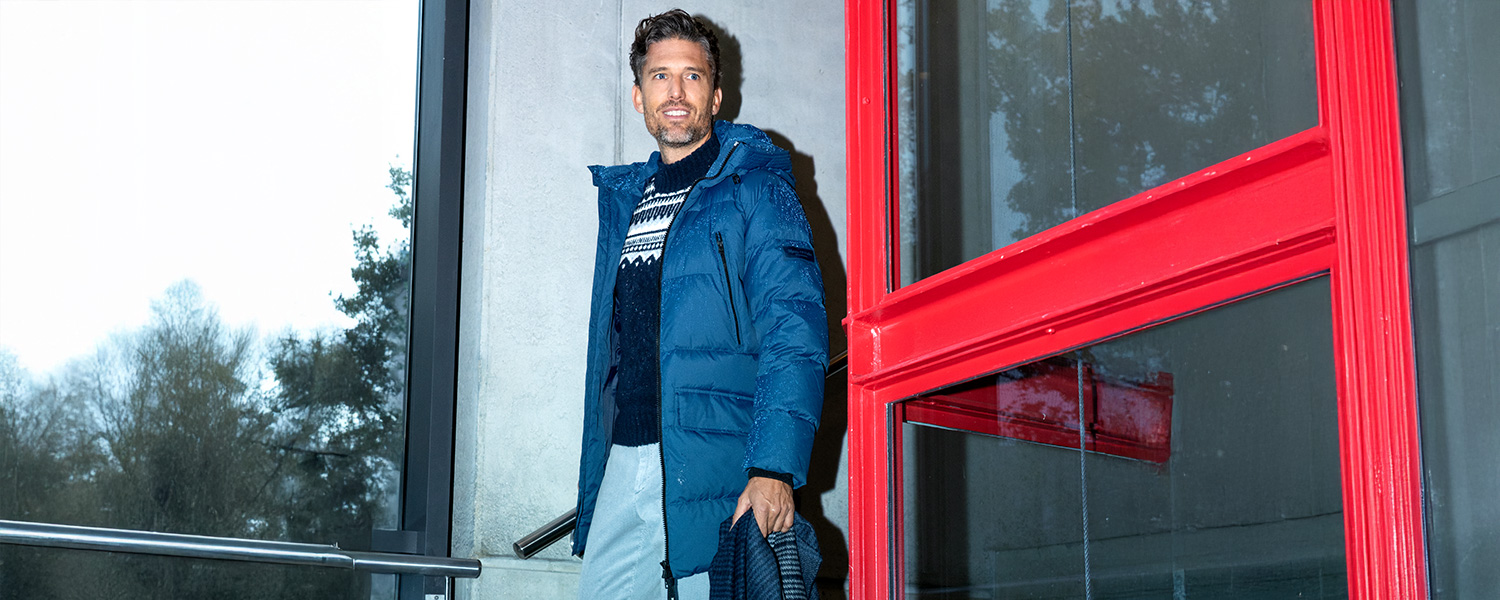 Mann in marineblauer Steppjacke mit Kapuze und Feinstrickpullover mit Muster