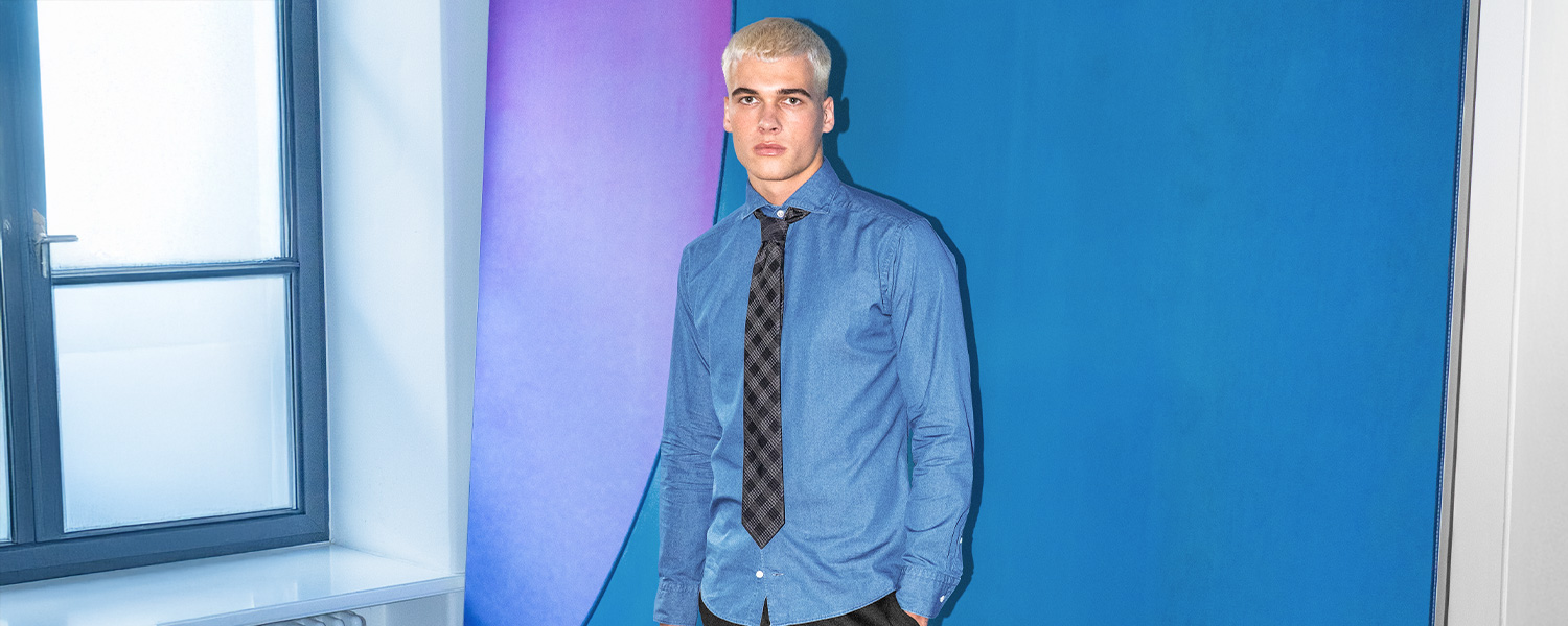 Mann in blauem Denim-Hemd mit schwarzer Krawatte vor blauem Hintergrund