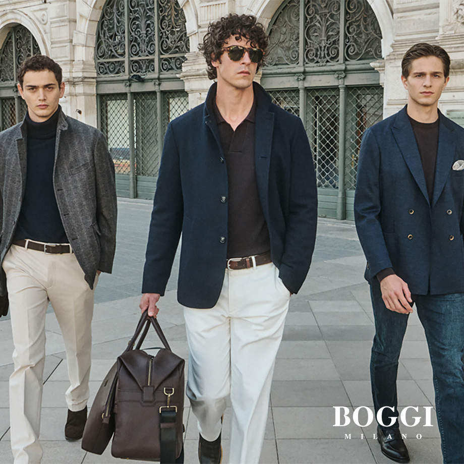 Drei Männer in Business-Sakkos mit dunklen Poloshirts und Chinos vor klassischer Architektur