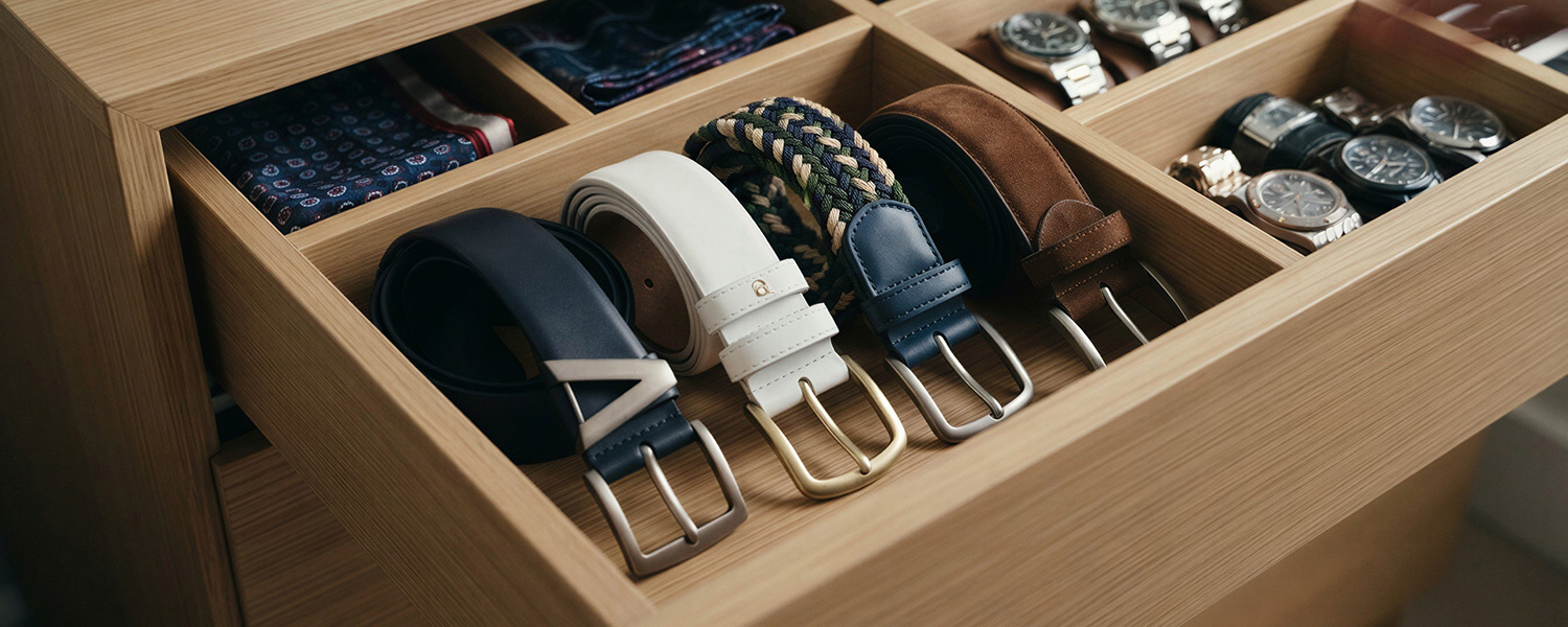 Herrengürtel in Leder und Textil sortiert in Holzschublade mit Krawatten und Armbanduhren