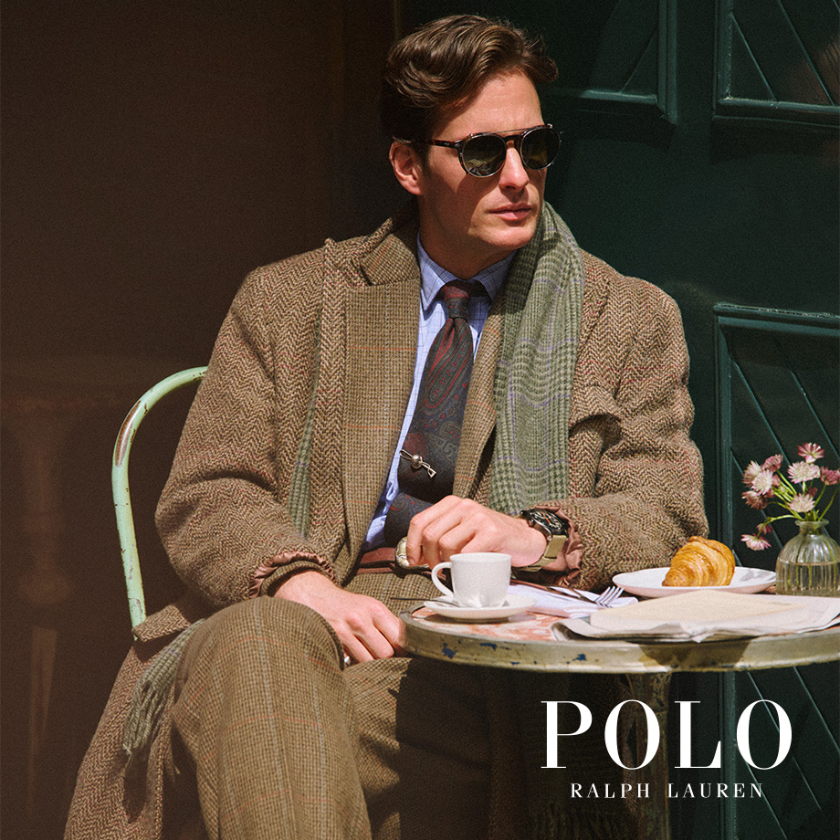 Mann in beigem Tweed-Anzug mit blauem Hemd und Krawatte beim Espresso im Café