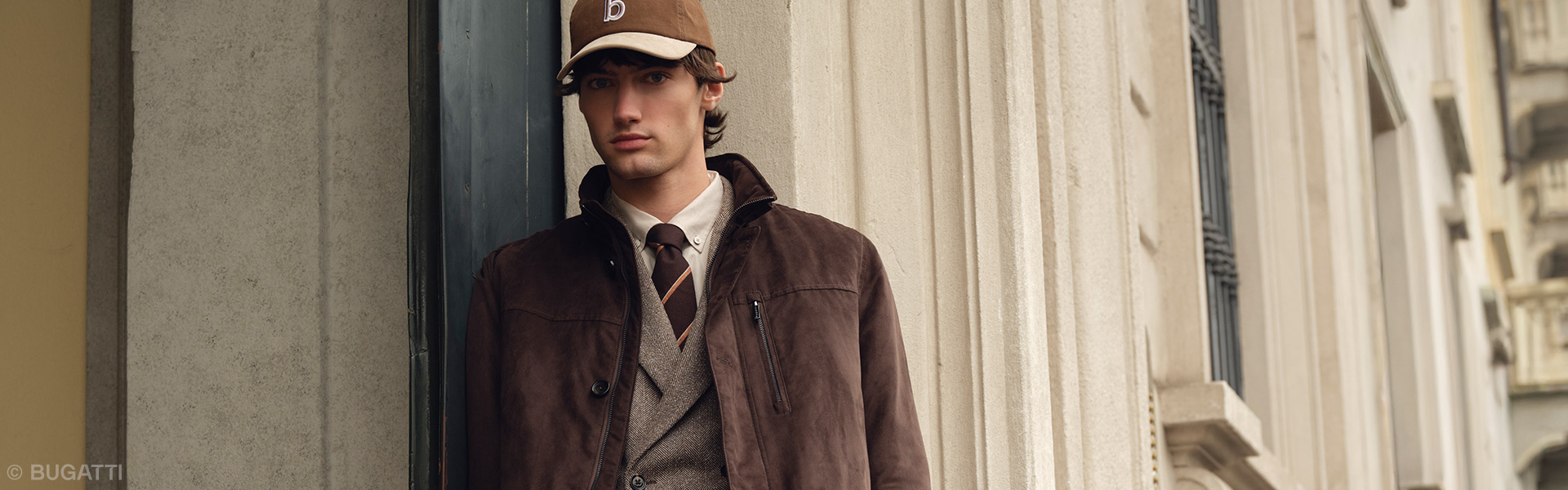Mann in brauner Wildlederjacke mit Strickweste, Hemd und Krawatte im eleganten Casual-Look