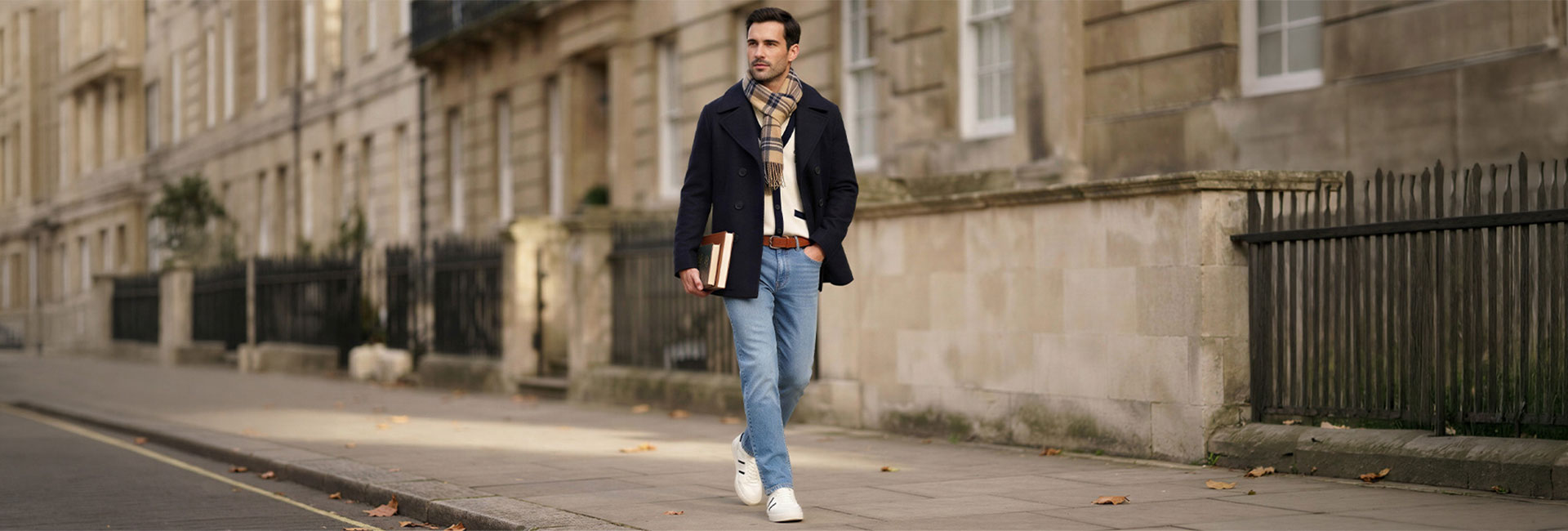 Mann in dunklem Wollmantel mit kariertem Schal und heller Jeans beim Spaziergang in der Stadt