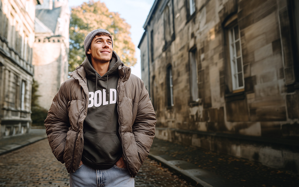 Mann in grauem Hoodie mit Schriftzug und brauner Steppjacke auf Straße