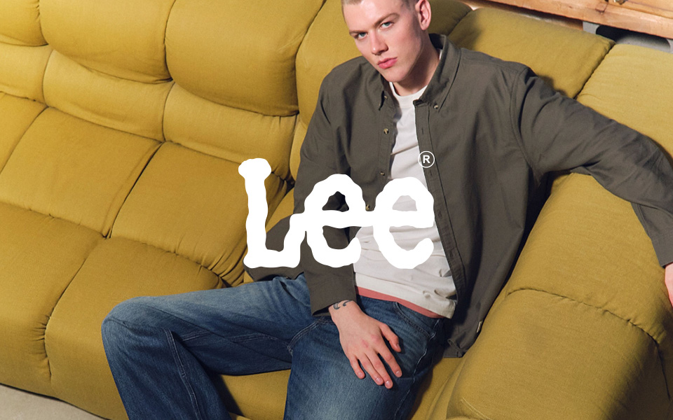 Casual-Look mit olivgrünem Hemd über weißem T-Shirt, kombiniert mit blauen Jeans auf gelbem Sofa sitzend