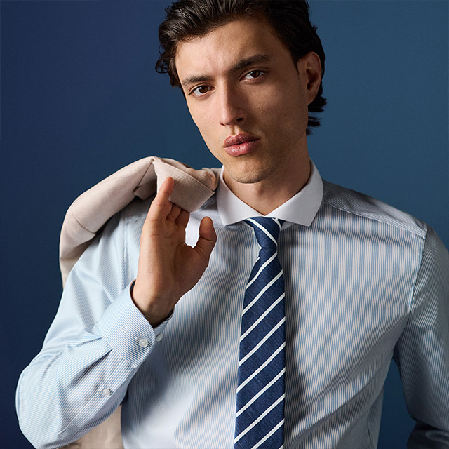 Mann in hellblauem Business-Hemd mit Streifen und blauer Krawatte, Sakko über Schulter