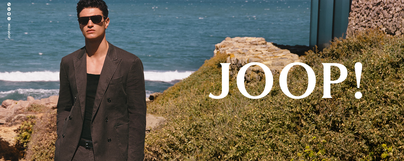 Mann im eleganten dunkelgrauen Anzug und Sonnenbrille, outdoor am Meer