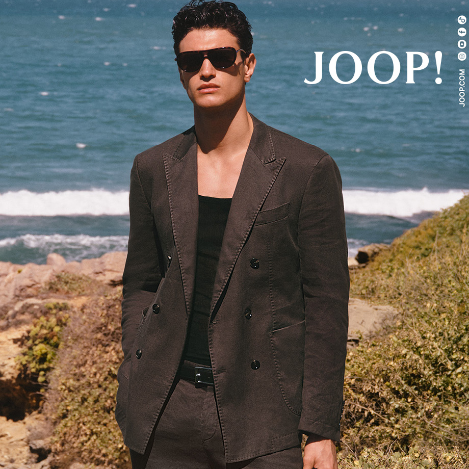 Mann in dunkelbraunem Anzug mit Sonnenbrille am Strand