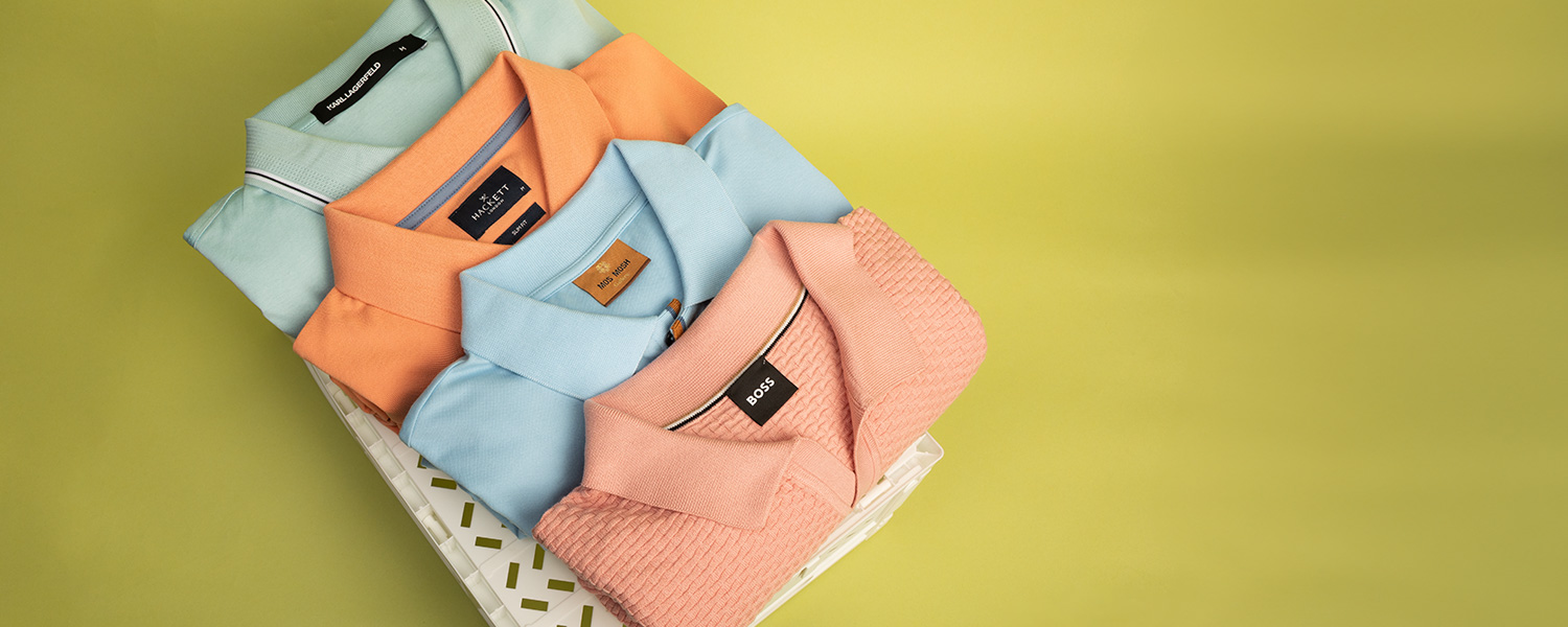 Hellblaue, orange und rosa Poloshirts aus Baumwolle, ordentlich gefaltet auf grüner Oberfläche