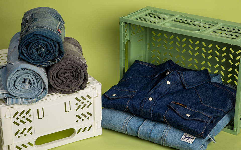 Gefaltetes Jeanshemd in Dunkelblau, gestapelt mit hellblauen Jeans vor grünem Hintergrund