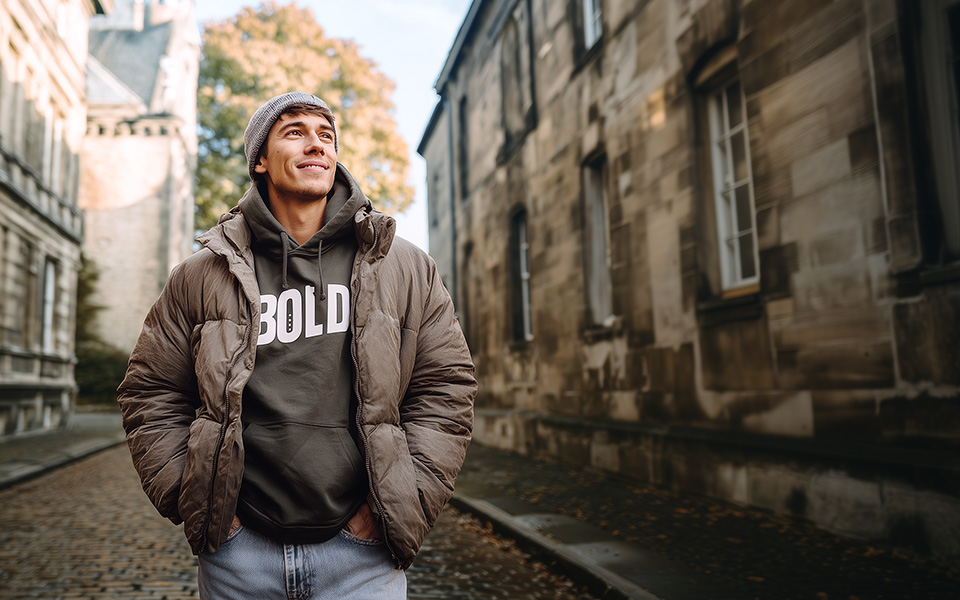 Mann in brauner Daunenjacke und grauem Hoodie auf Kopfsteinpflasterstraße