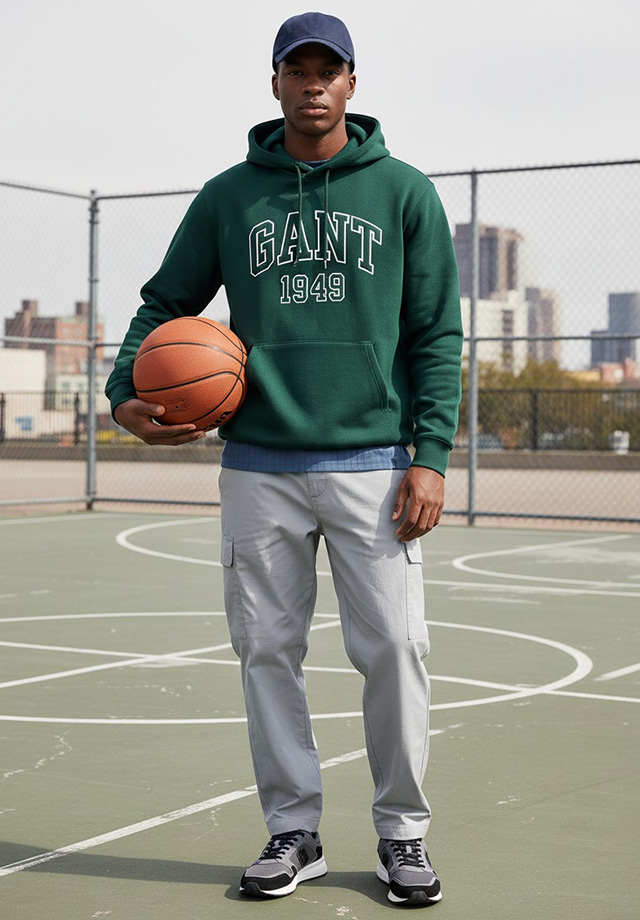 Mann in grünem Hoodie mit Schriftzug, hellgraue Cargohose, sportlich auf Basketballplatz