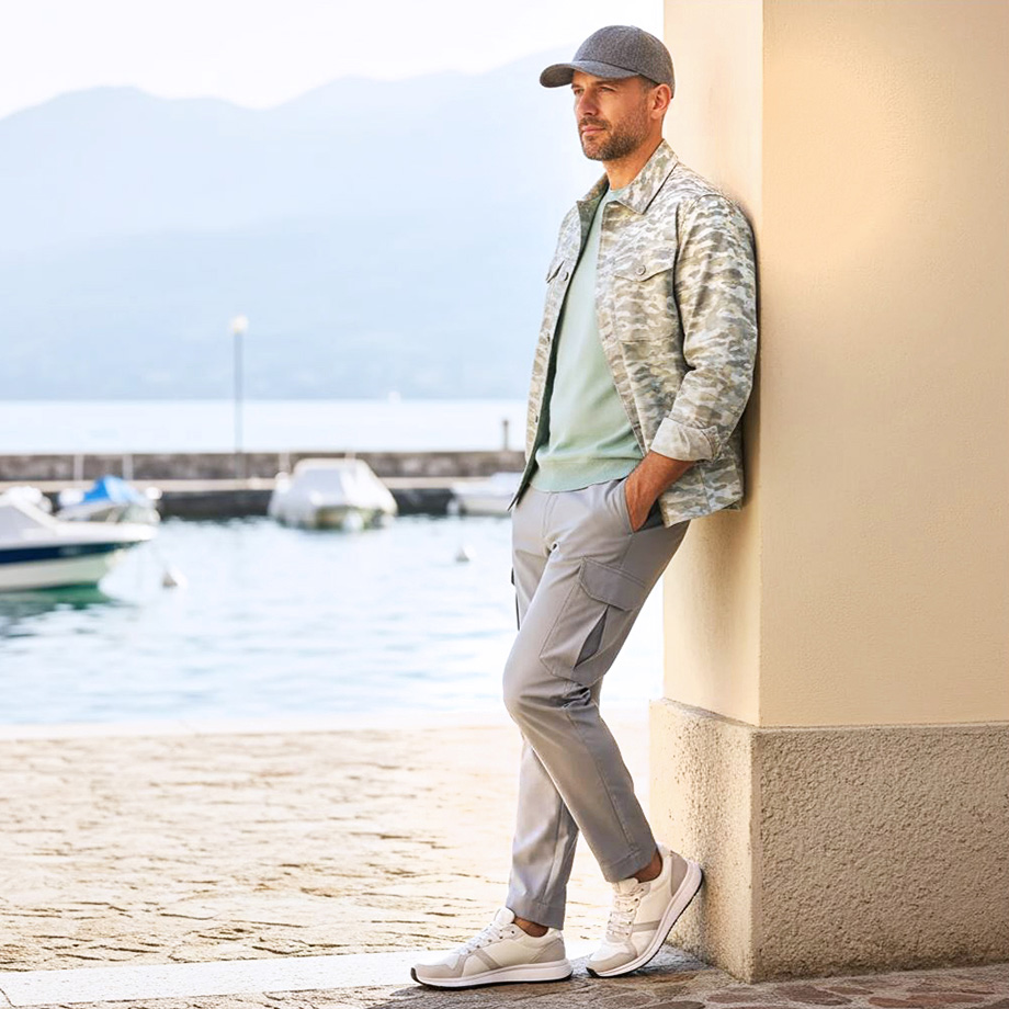 Mann in grauem Freizeit-Outfit mit Cargohose und Turnschuhen, am Wasser stehend