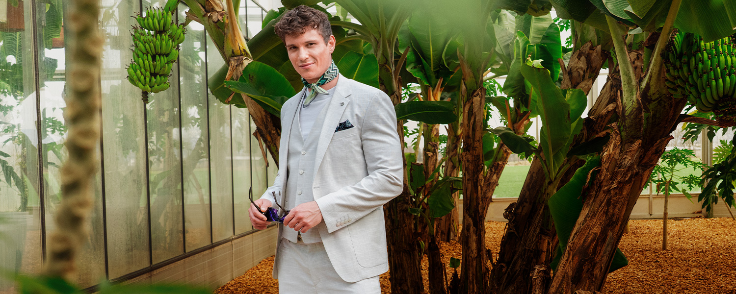 Mann im dunkelvioletten Dreiteiler mit Weste und blau gestreifter Krawatte, klassisch getragen vor Lokomotive.