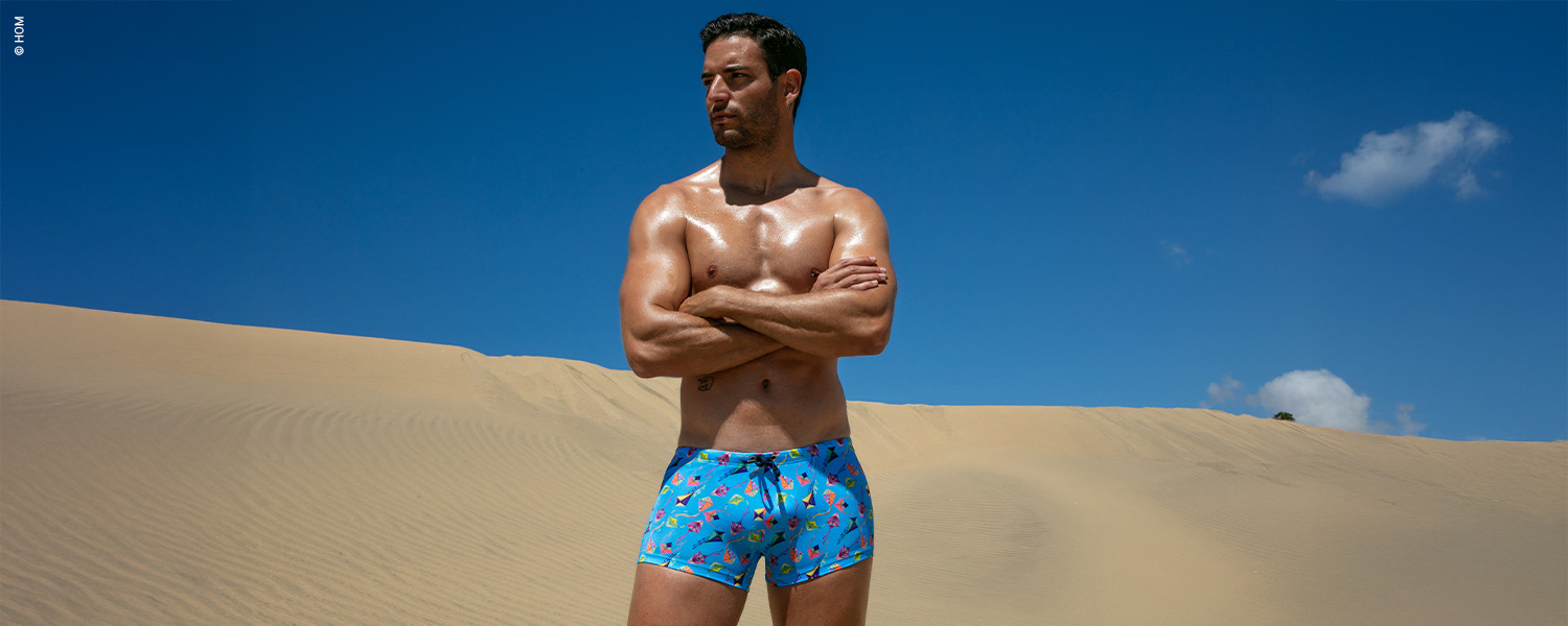 Mann in blauer gemusterter Badehose in der Wüste stehend