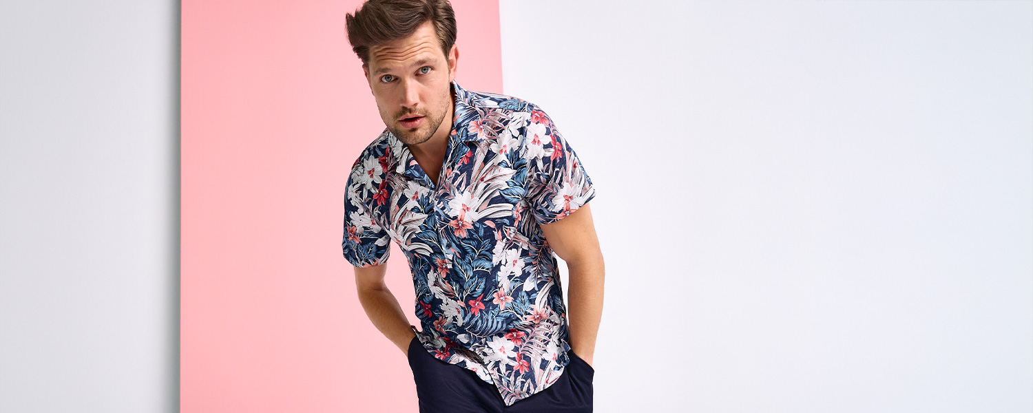 Herr in floral bedrucktem Kurzarmhemd aus Baumwolle vor rosa Hintergrund