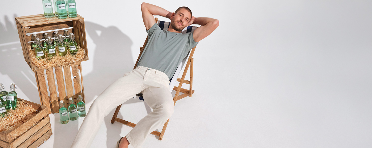 Mann in grauem T-Shirt und weißen Hosen entspannt auf Liegestuhl, lässige Sommermode