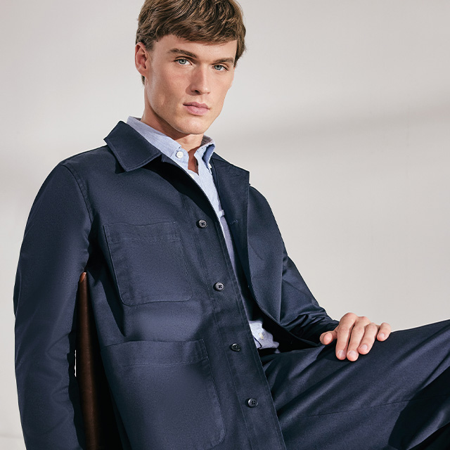 Eleganter Mann in dunkelblauer Anzugjacke und Hemd, sitzend im Studio