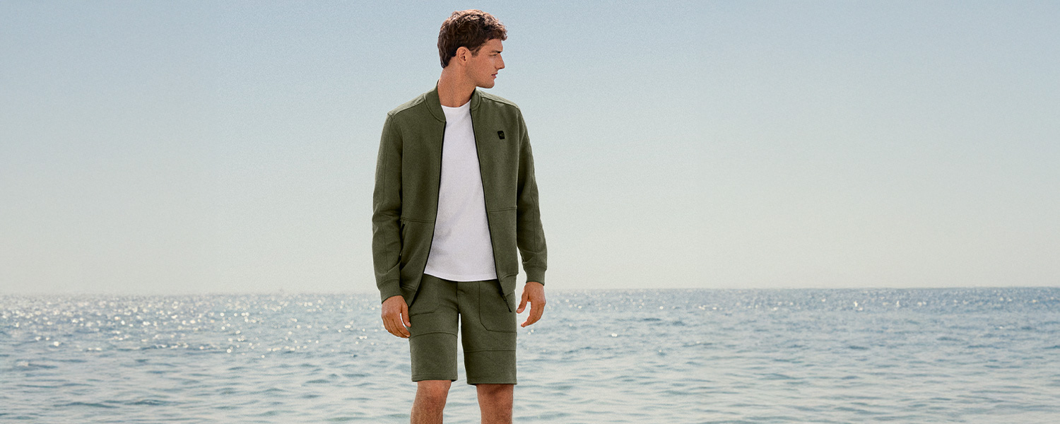 Mann in olivgrüner Freizeitjacke und Shorts am Meer, lässig getragen