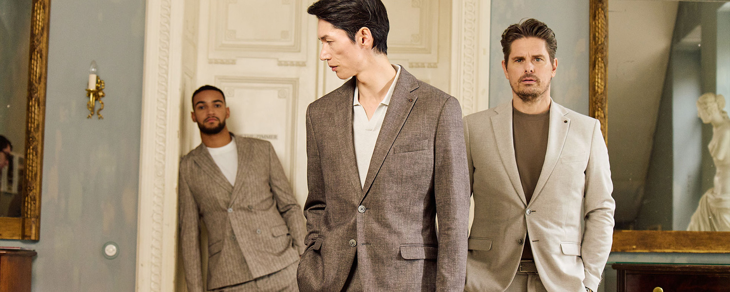 Herren in eleganten Anzügen aus Wolle, beige und braun, klassisch geschnitten, in stilvollem Ambiente