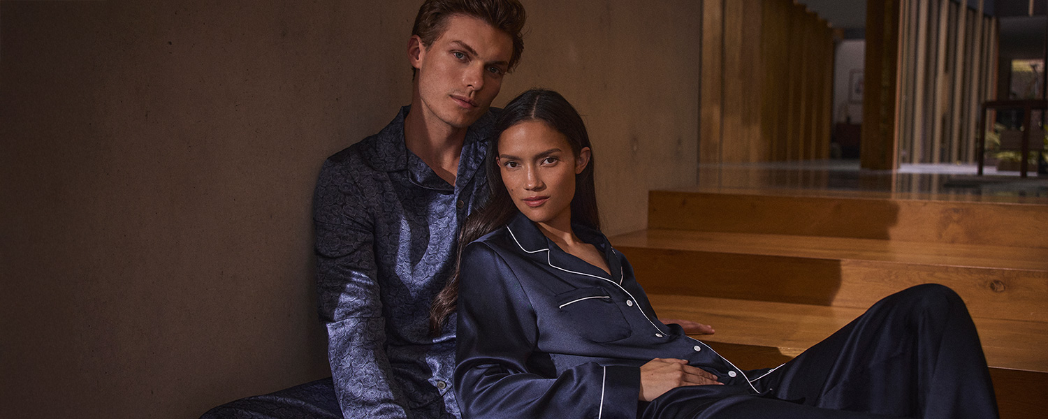 Mann in dunkelblauem Pyjama mit floralem Muster, elegant sitzend auf Holztreppe