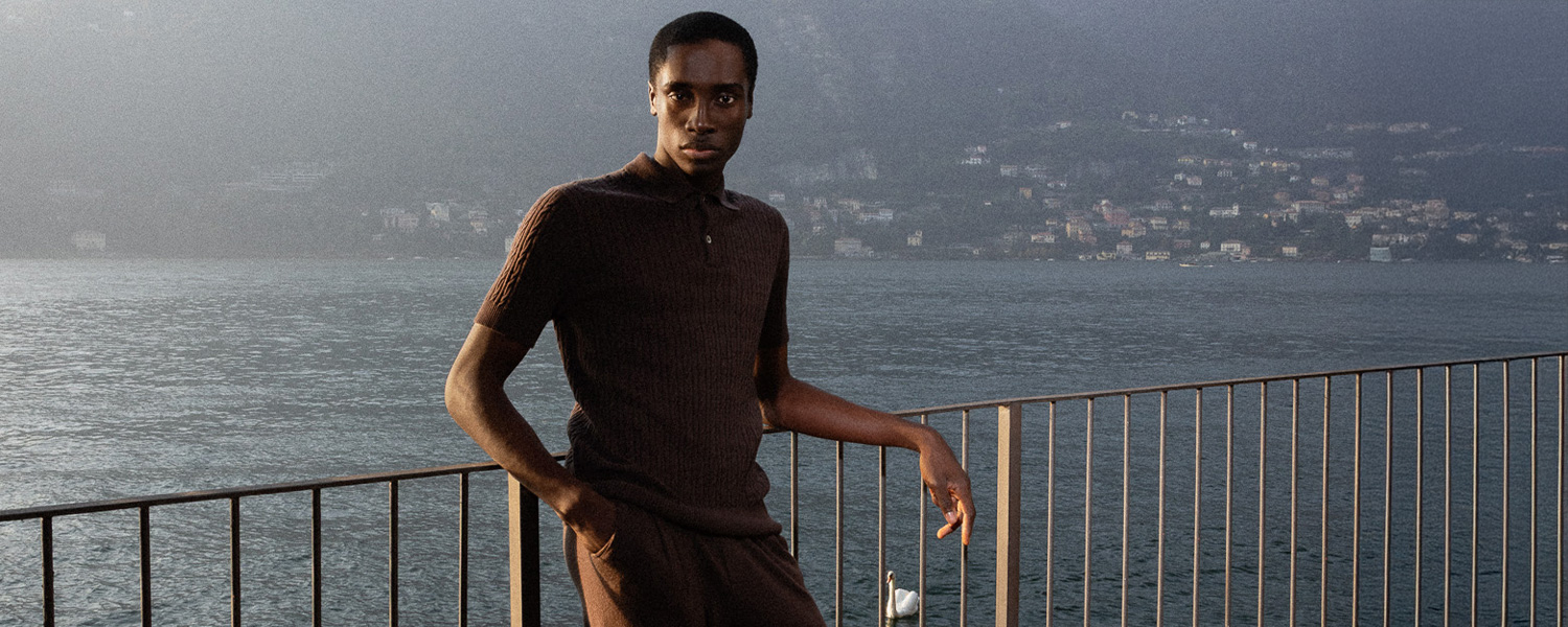 Dunkelbraunes Strickpoloshirt aus Baumwolle, lässig getragen vor malerischer Seelandschaft