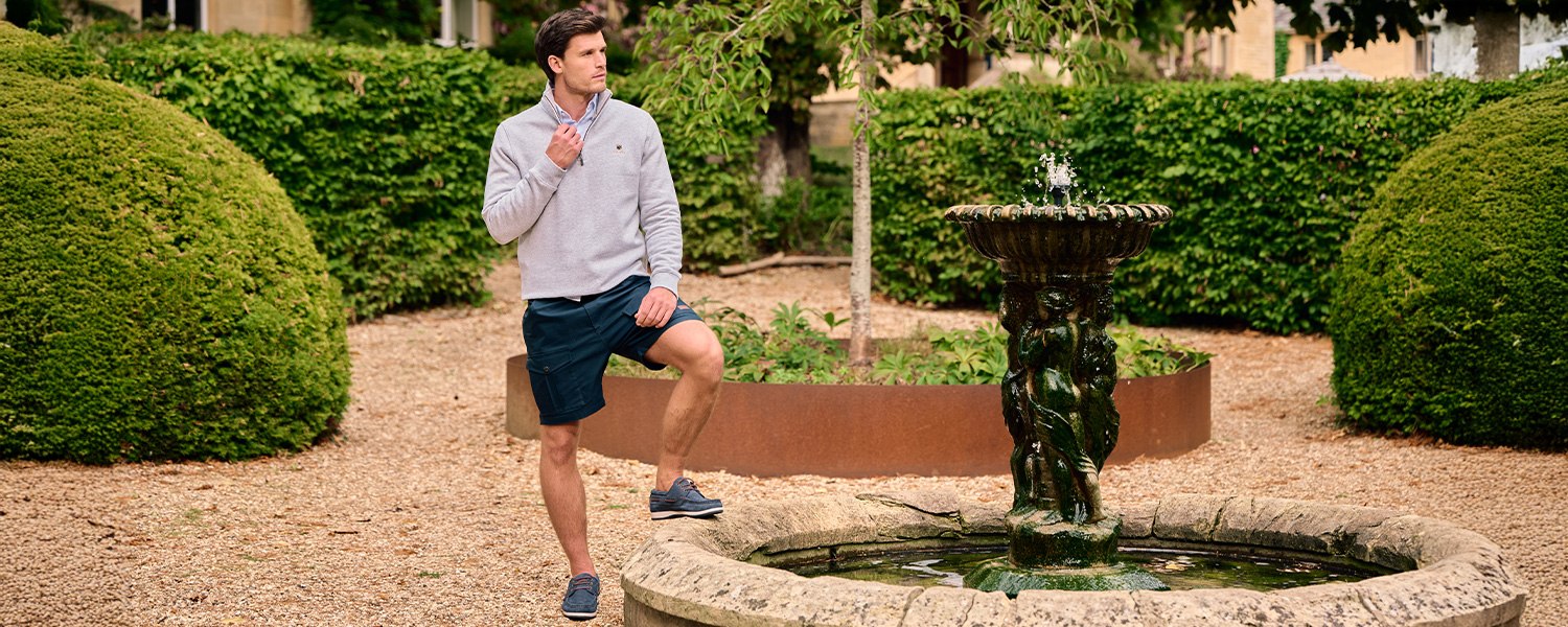 Mann in grauem Pullover und blauen Shorts entspannt im Garten, Freizeitlook