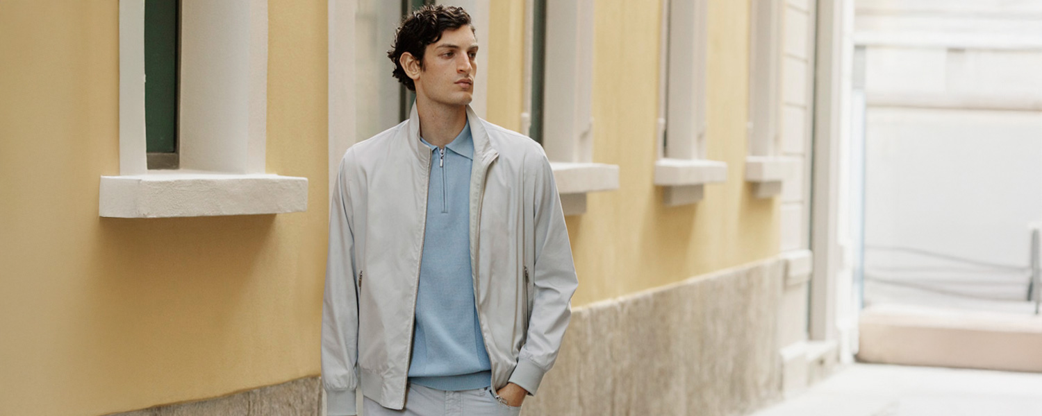 Mann in hellgrauer Bomberjacke und hellblauem Poloshirt im Freien