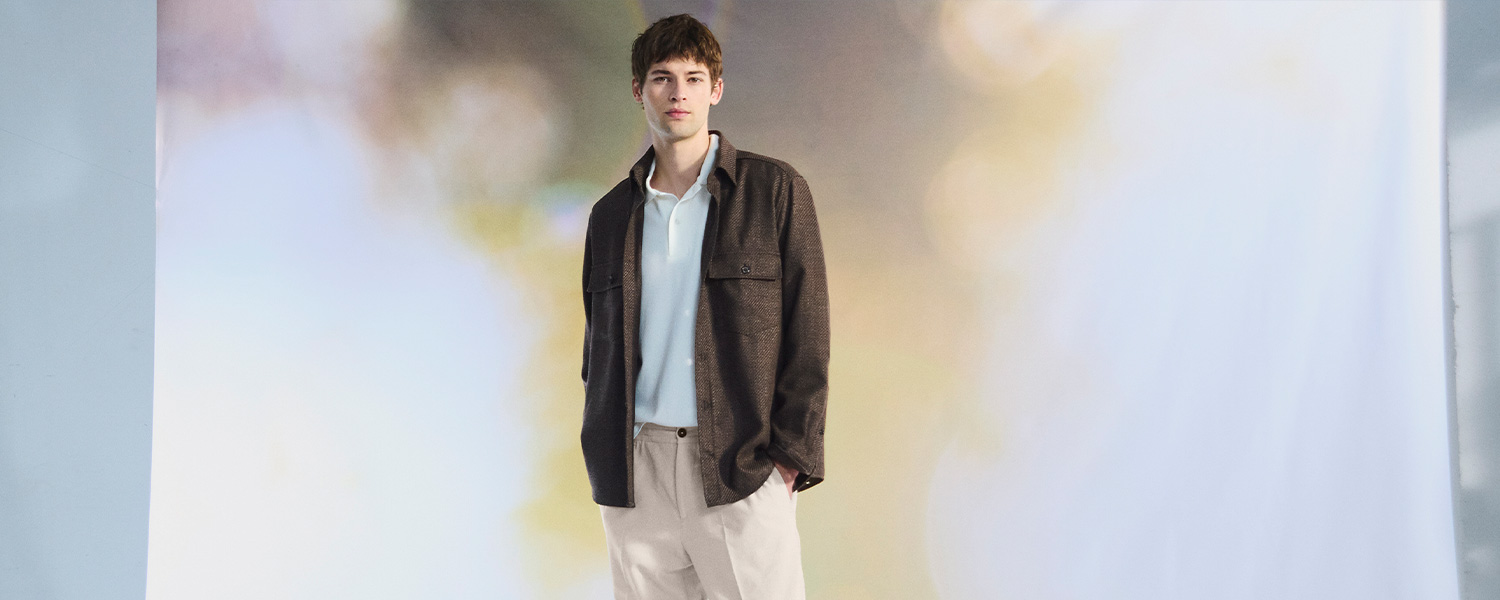 Elegante braune Jacke über hellblauem Hemd, lässig getragen zu beigen Hosen im Studio