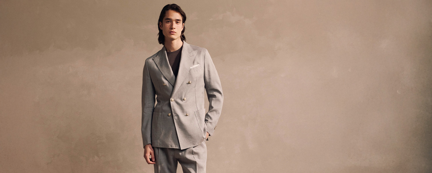 Mann in grauem Anzug mit Doppelreiher, elegant präsentiert vor neutralem Hintergrund