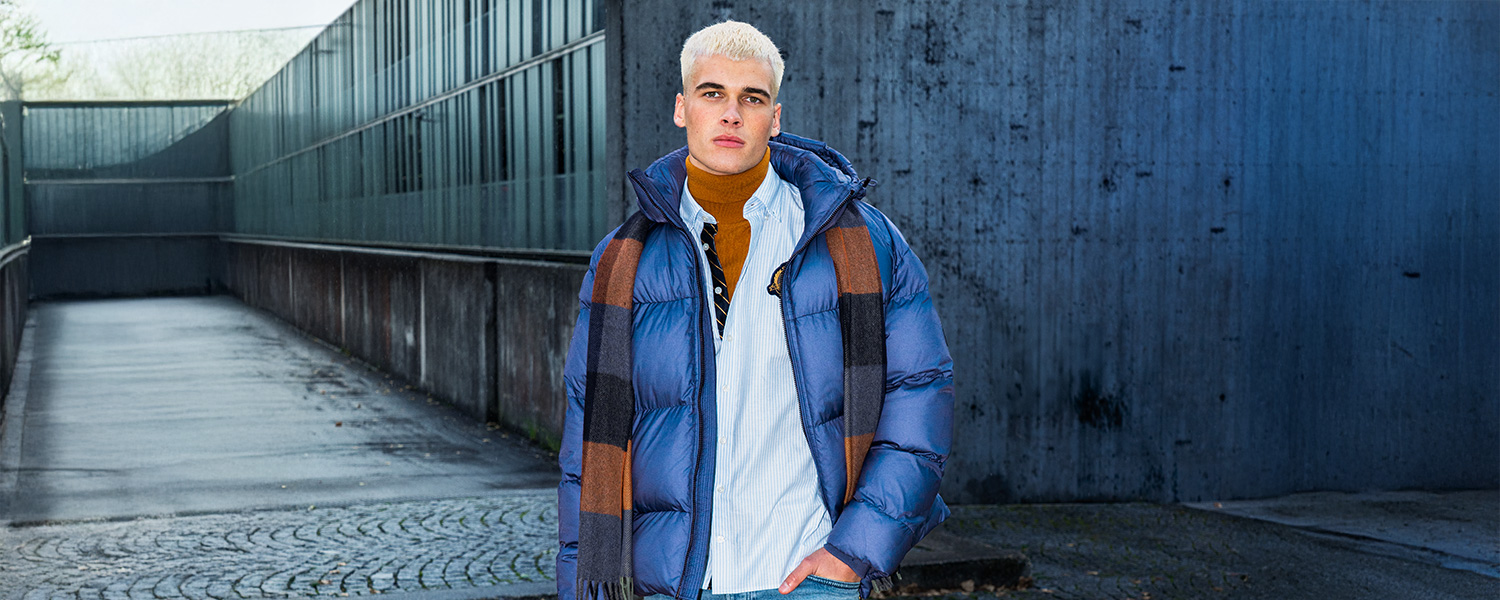 Mann in gesteppter blauer Winterjacke mit Streifenschal, lässig gestylt in urbaner Umgebung