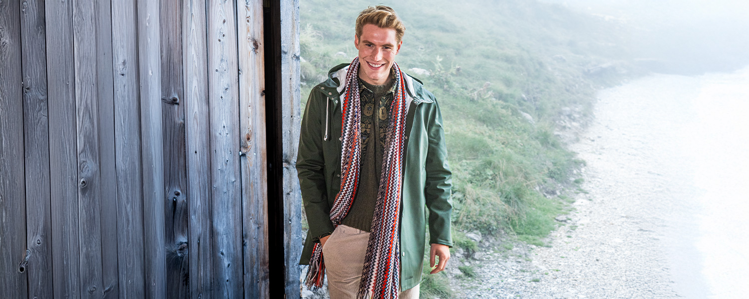 Grüne Herren-Regenjacke mit Kapuze, kombiniert mit Schal und Freizeitlook – stilvoller Wetterschutz für regnerische Tage.