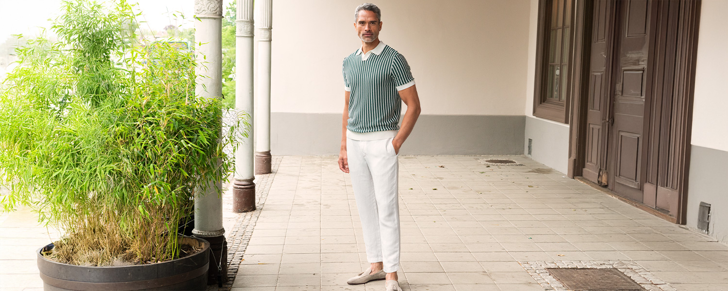 Weiße Stoffhose in geradem Schnitt, kombiniert mit grün gemustertem Poloshirt und Loafern im Sommerlook.
