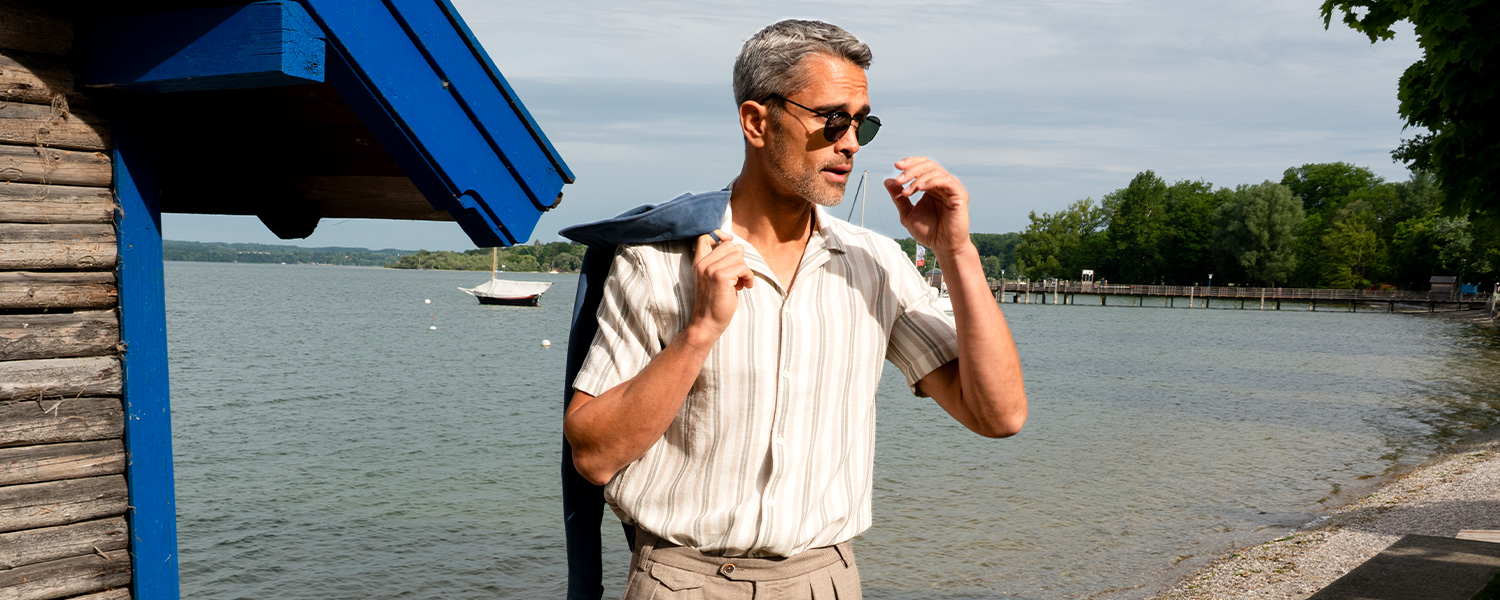Mann mit blau-weiß gestreiftem Hemd und grünem Anzug steht in nebliger Berglandschaft – eleganter Outdoor-Look für Herbst und Winter.