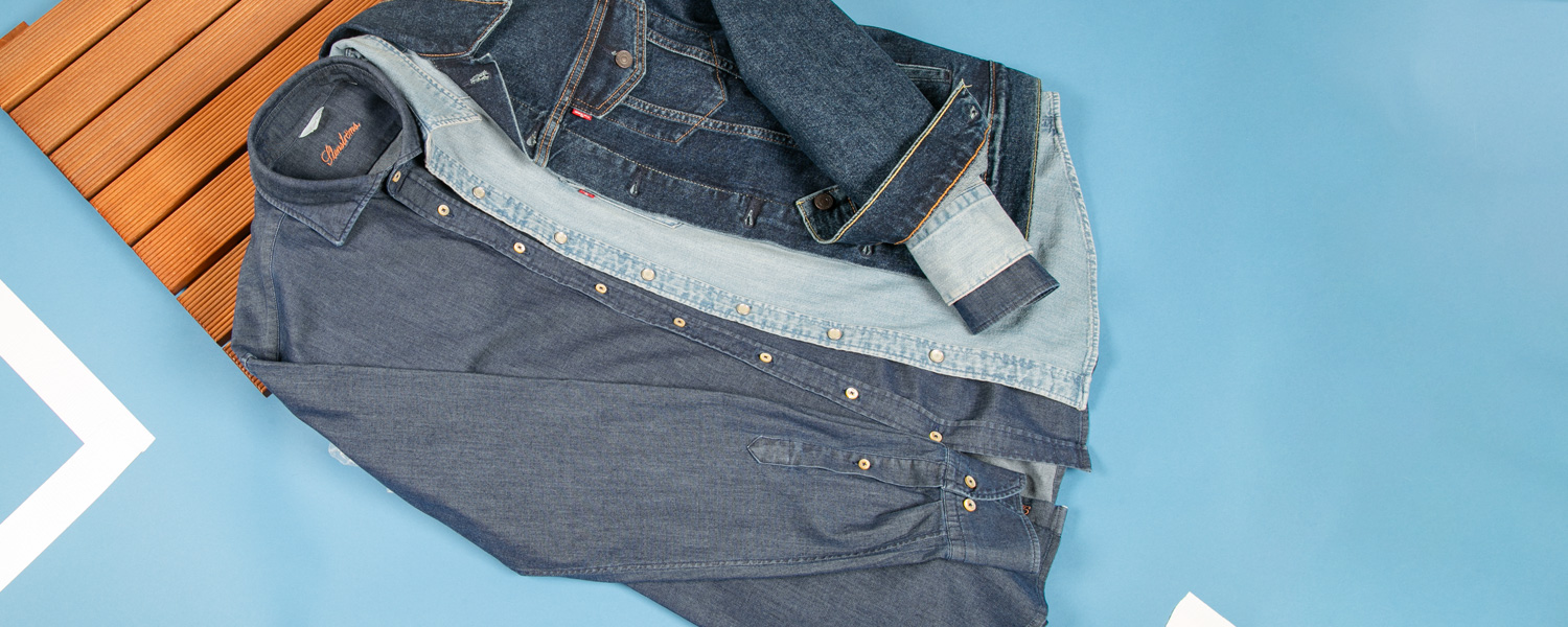 Blaues Jeanshemd in Kombination mit grauer Strickweste und brauner Wildlederjacke, getragen im Outdoor-Setting.