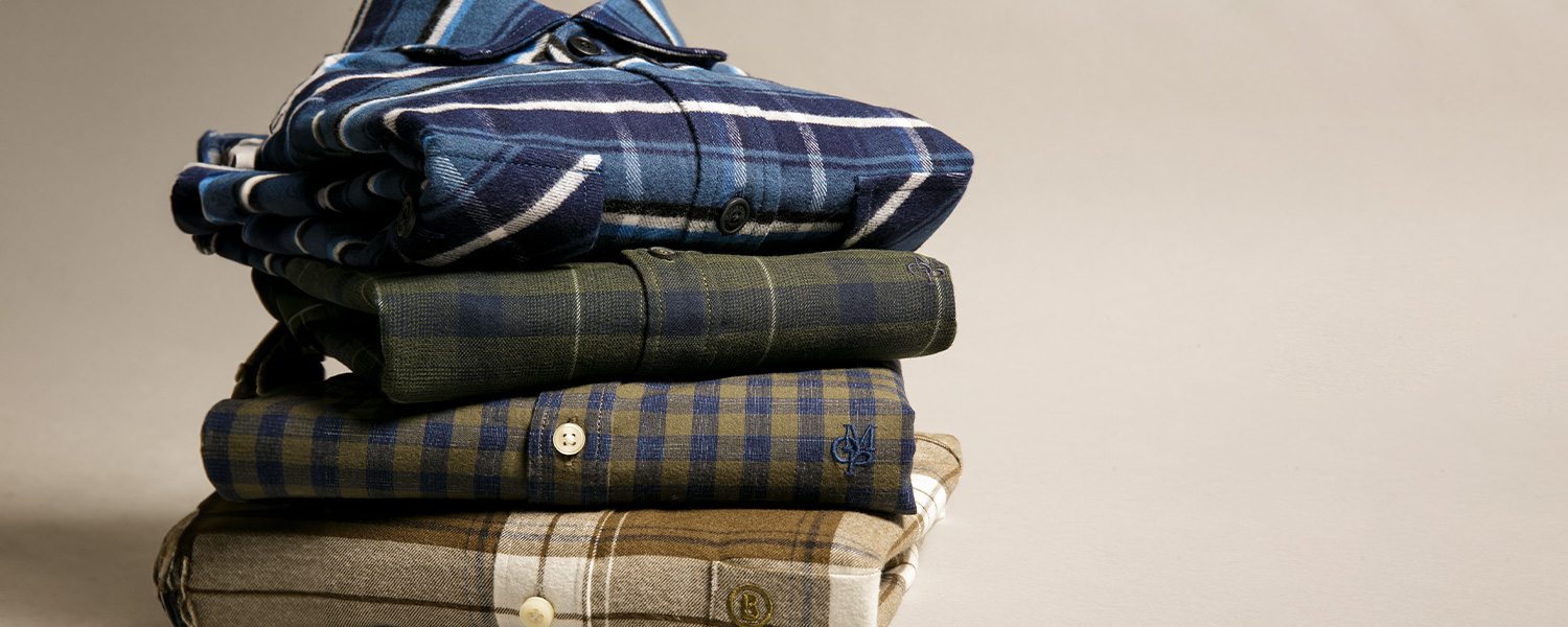 Gestapelte Karohemden in Blau, Grün und Braun, aus Baumwolle gefaltet und liegend präsentiert.