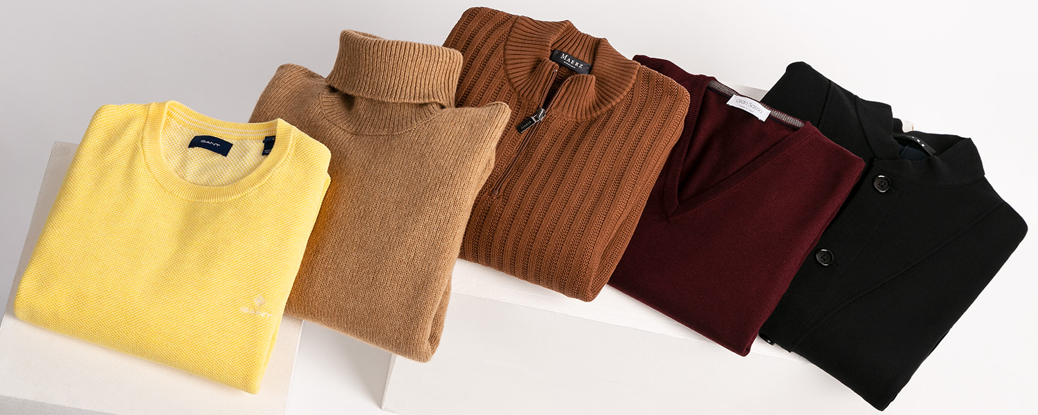 Auf dem Bild trägt ein Mann einen beigefarbenen Troyer mit halbem Zipper unter einer schwarzen Steppjacke.