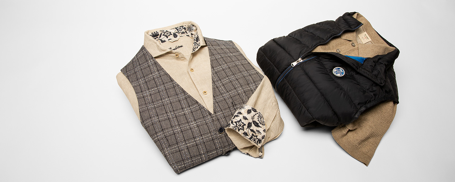 Auf dem Bild sitzt ein Mann auf einem Sofa und trägt einen schwarzen Strick-Pullunder kombiniert mit einer hellen Jeans.