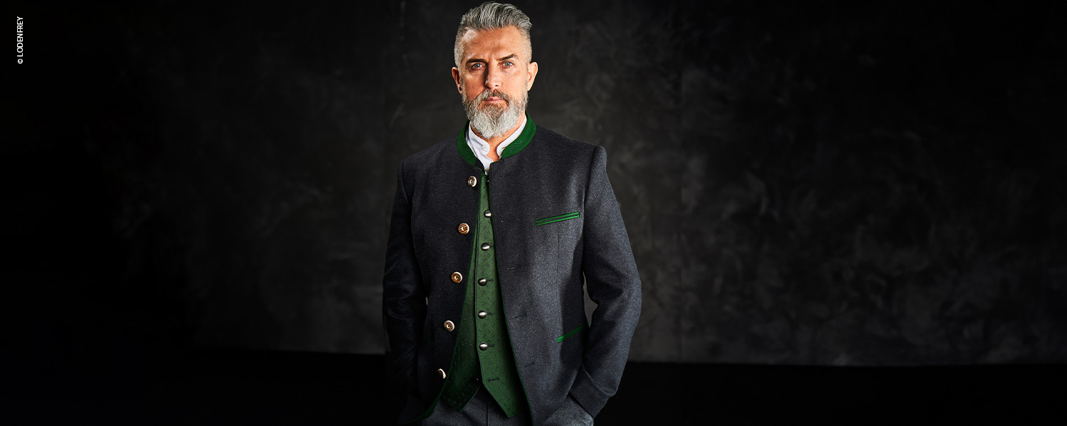 Auf dem Bild ist ein Mann in einem eleganten Trachtensakko mit grünen Akzenten und silbernen Knöpfen zu sehen – traditionell und stilvoll kombiniert.
