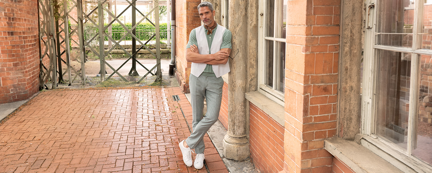 Graue und beige Business-Hosen in Kombination mit Strickpullovern und Mänteln, getragen im entspannten Indoor-Look.